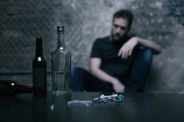 Long Term Health Effects of Drug Abuse - man sitting in the shadows with drugs on the table