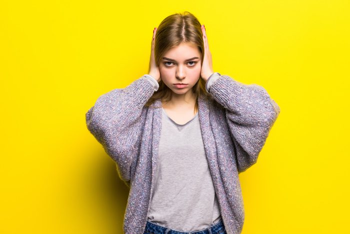 girl with hands over ears on yellow background