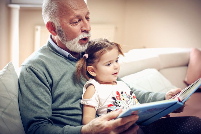 grandfather reading story with young granddaughter in his lap - books