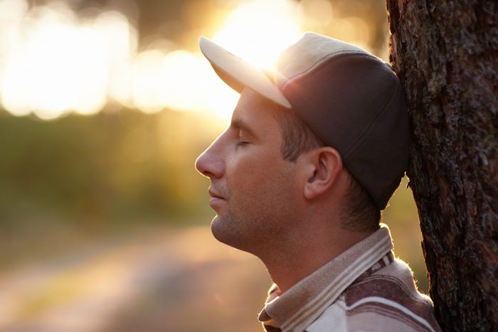 young man in baseball cap leaning against a tree with his eyes closed - urge surfing