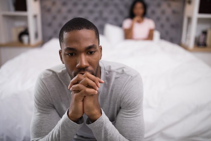 handsome African American man looking concerned sitting on edge of his bed - sexual dysfunction