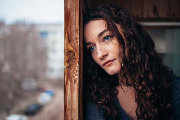 sad beautiful woman leaning against wall looking out window - self-talk